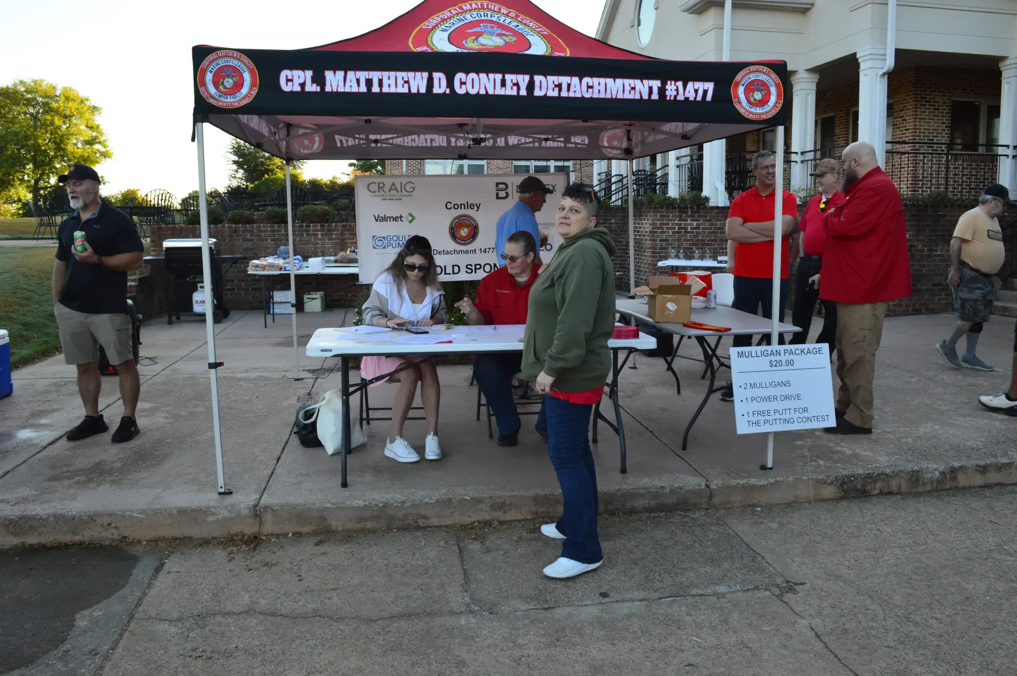 Volunteers at the Conley Detachment 1477 check-in tent at the golf tournament, with a sign advertising the Mulligan Package