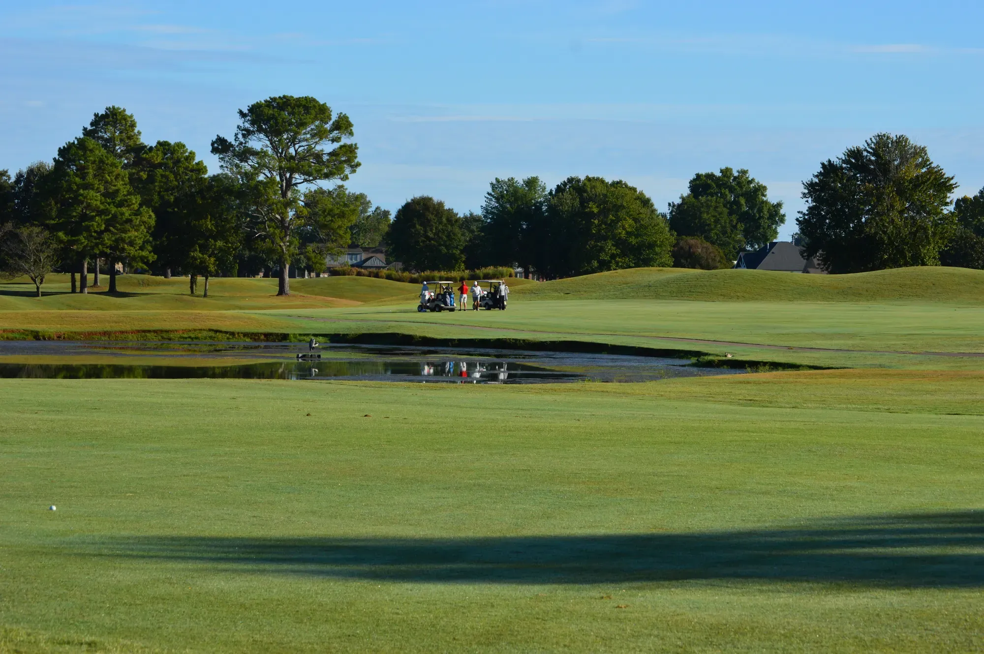 Golf carts and players beside a pond on the fairway at Cypress Lake under a blue sky