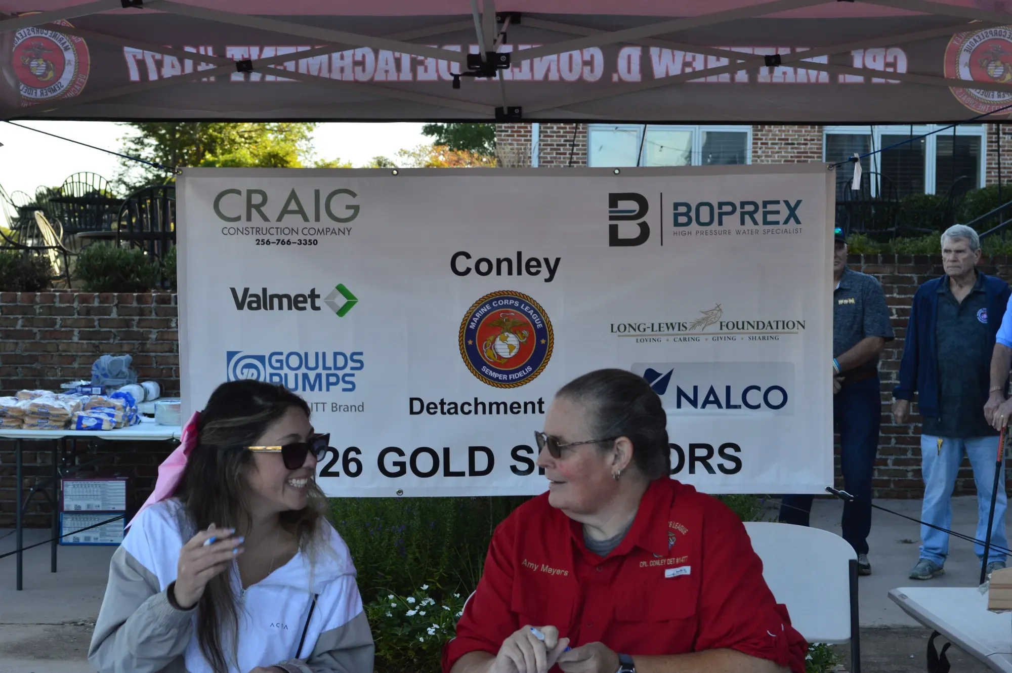 Volunteers seated at the sign-in table in front of a banner listing the 2026 Gold Sponsors
