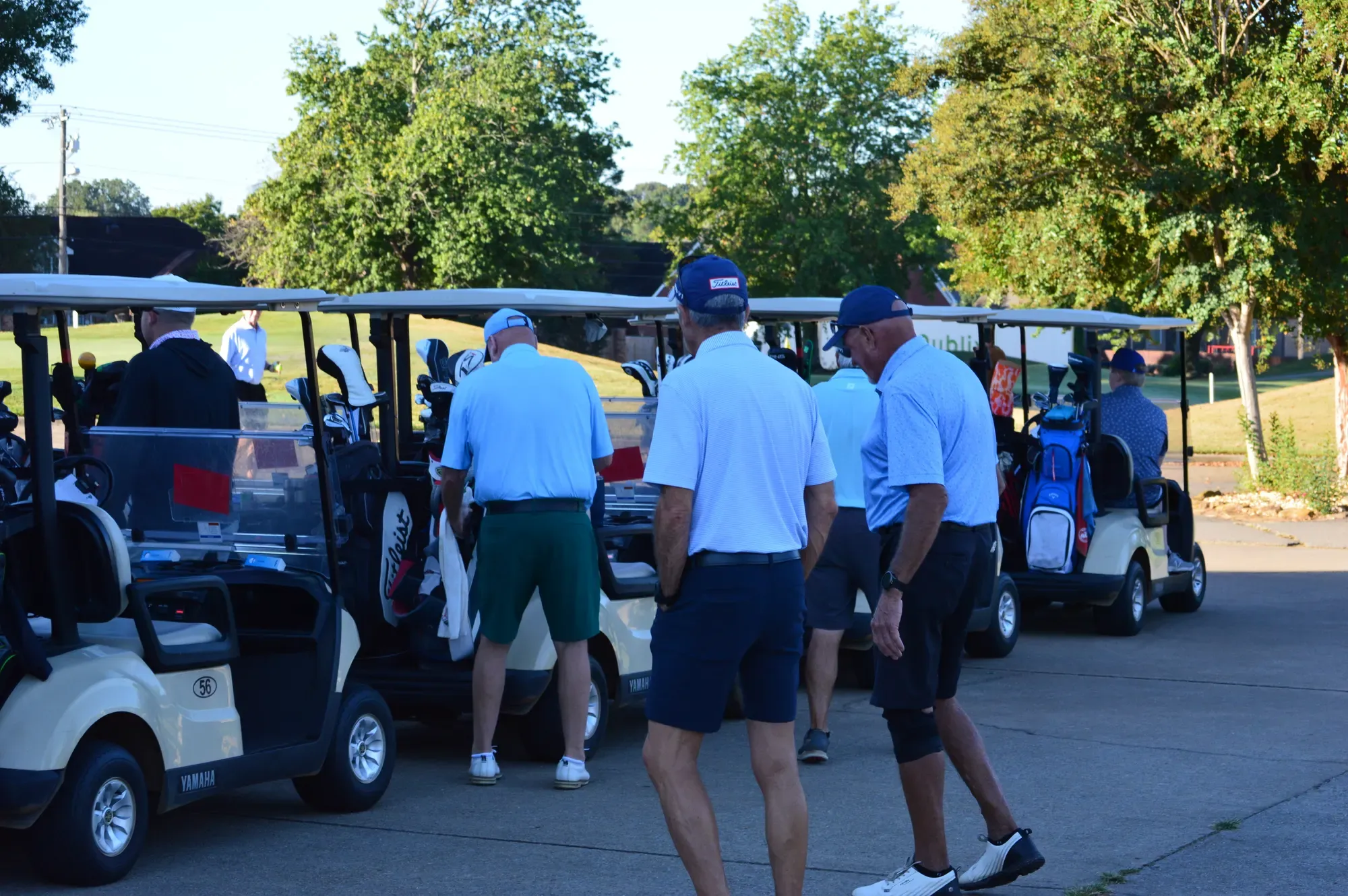 Golfers in light blue shirts gather beside a row of golf carts in the early morning light