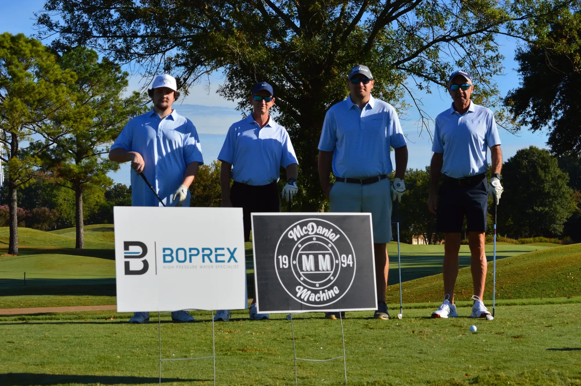 A four-person team in matching red shirts holding golf clubs on the course